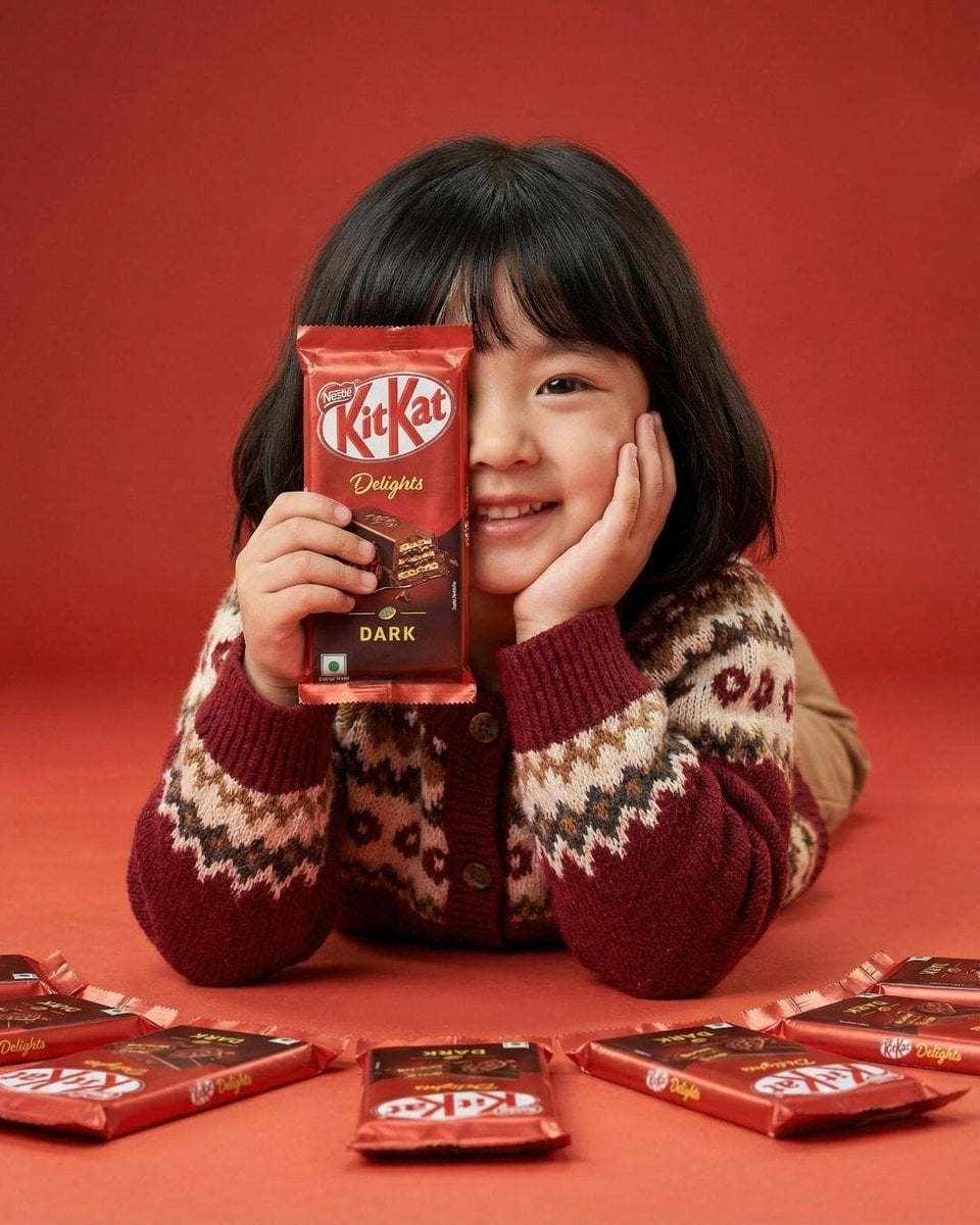 A cute young girl with short black hair and bangs smiling while holding a red KitKat Dark...