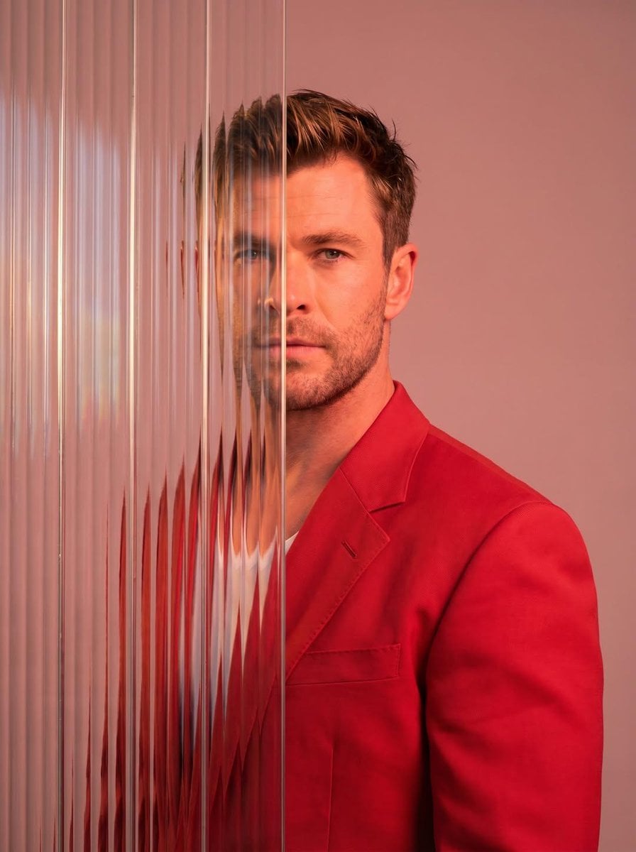 A striking editorial portrait photograph of a person wearing a red blazer, shot against a...